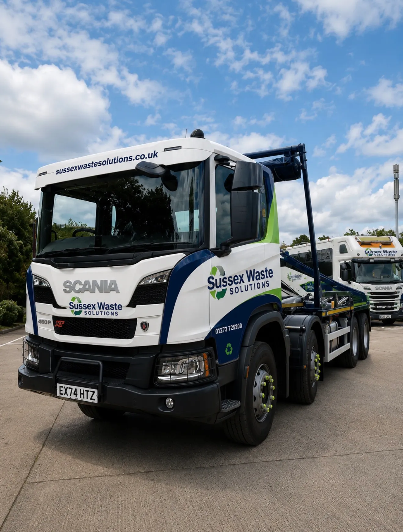 White and blue Sussex Waste Solutions Scania truck parked on concrete under a partly cloudy sky.
