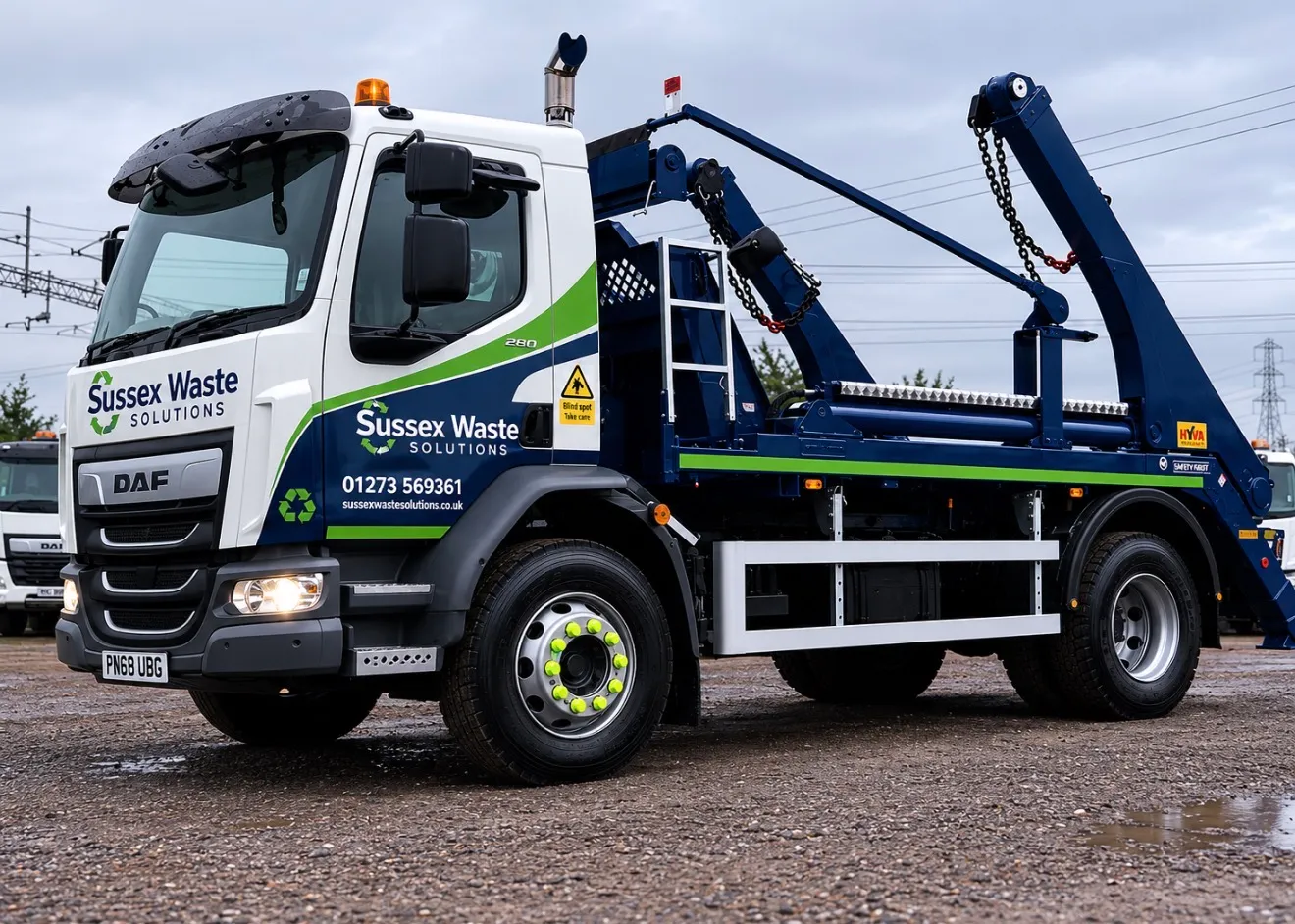 Sussex Waste Solutions skip-lift truck parked on gravel with white and blue cab and green accents.